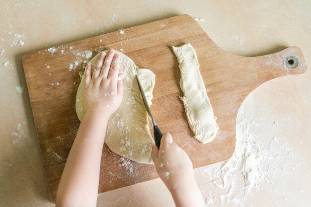 Kinderhände, die rohen gerollten Teig schneiden