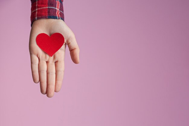 Kinderhände, die rotes Papierherz in den Händen auf rosa Hintergrund halten. Valentinstag, Muttertag und Liebe Konzepte.