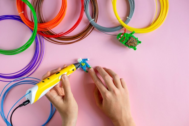 Kinderhände erstellen Figuren mit einem 3D-Stift auf der rosa Hintergrund-Draufsicht