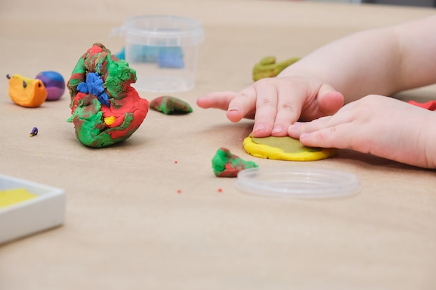 Kinderhände formen einen Kreis aus gelbem Plastilin, ein Mädchen spielt mit Plastilin am Tisch