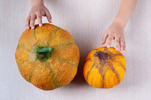 Kinderhände halten einen hausgemachten orangefarbenen Pappmaché-Kürbis für Halloween auf einem Tisch, Flatley