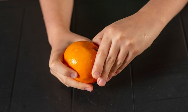Kinderhände schälen eine Mandarine über dem Tisch