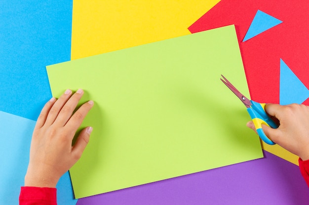Kinderhände schneiden farbiges Papier mit einer Schere