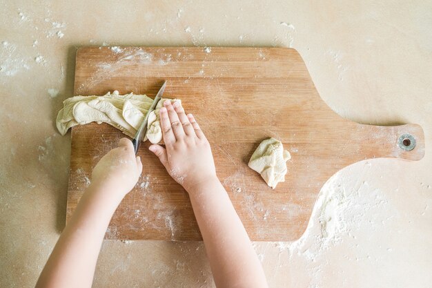 Kinderhände schneiden rohen Teig