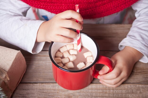 Kinderhand, die roten Becher Weihnachtskakao auf dem Holztisch hält