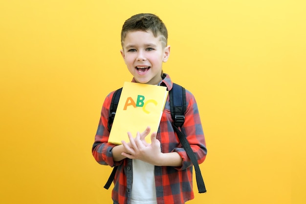 Kinderjunge auf gelbem Wandhintergrund Tolle Idee Fröhlicher lächelnder Schuljunge geht zurück zur Schule Erfolgsmotivationsgewinner Genius-Konzept Lehrbuch in der Hand