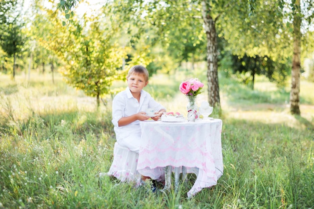 Kinderjunge, der an einem Tisch in der Natur sitzt. Tee trinken