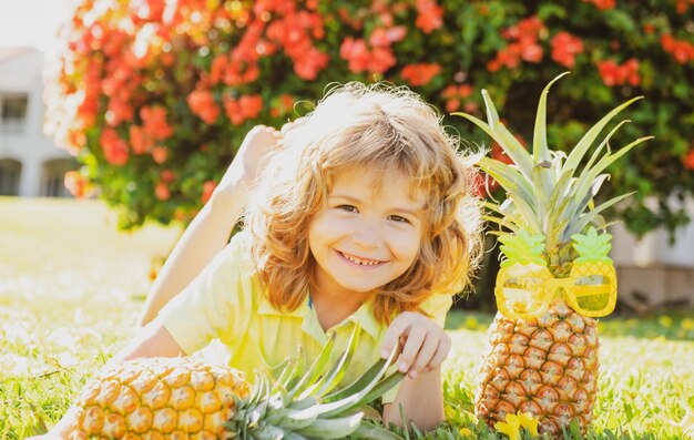 Kinderjunge, der Ananas hält, die mit Sommerfrüchten des glücklichen Gesichtes lächelt