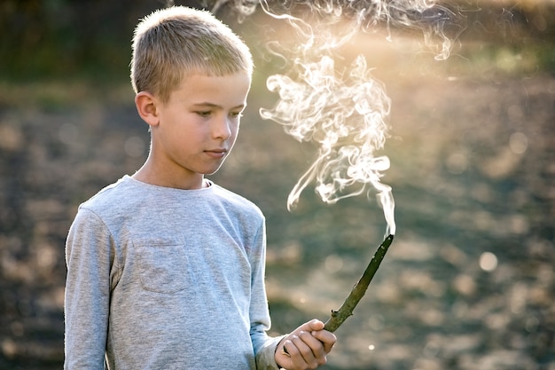 Kinderjunge, der draußen mit rauchendem Holzstock spielt.