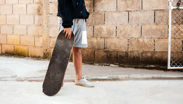 Kinderjunge, der ein Skateboard mit einem braunen Hund auf dem Zementboden hält