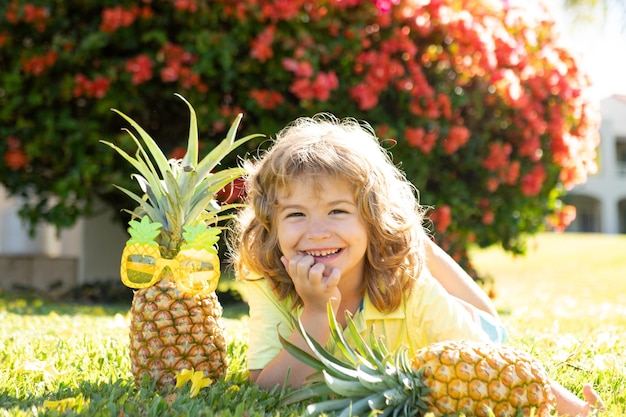 Kinderjunge, der eine Ananas hält, die Sommernaturhintergrund mit Kopienraum aufwirft Gesunde Früchte für Kinderkonzept