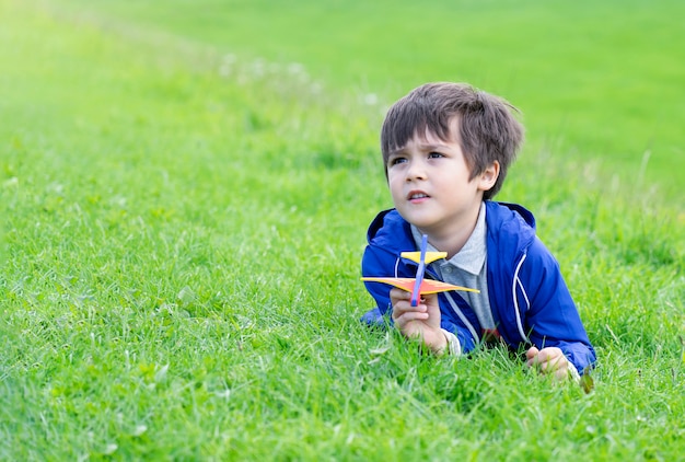 Kinderjunge, der sich auf grünem gras hinlegt und oben mit neugierigem gesicht schaut