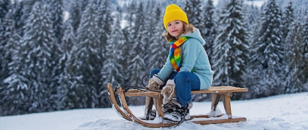 Kinderjunge, der Spaß mit einem Schlitten auf der Winterlandschaft hat süße Kinder, die im Schnee auf verschneiter Natur spielen