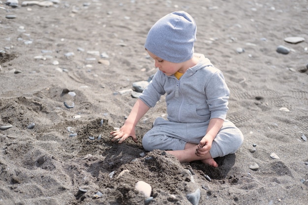 Kinderjunge faltet Burg aus Steinen, spielt an einem sonnigen Tag mit Felsen am Ufer.