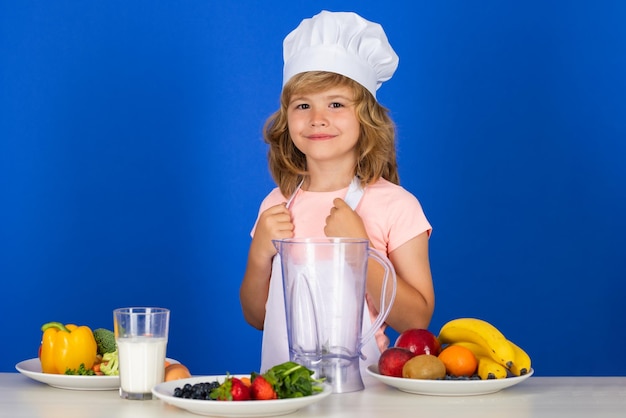Kinderjunge in Kochmütze und Schürze, die Mahlzeit zubereitet, kleiner Koch mit Gemüse in der Küche obst a