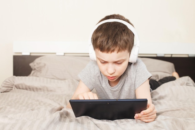 Kinderjunge liegt zu Hause mit PC-Tablet auf dem Bett und liest online