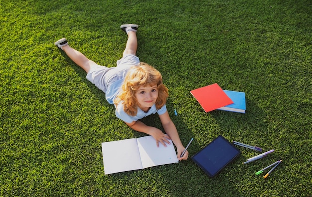 Kinderjunge liest Zinsbuch und schreibt auf Notizbuch im Garten Sommerspaß süßer Junge liegt auf