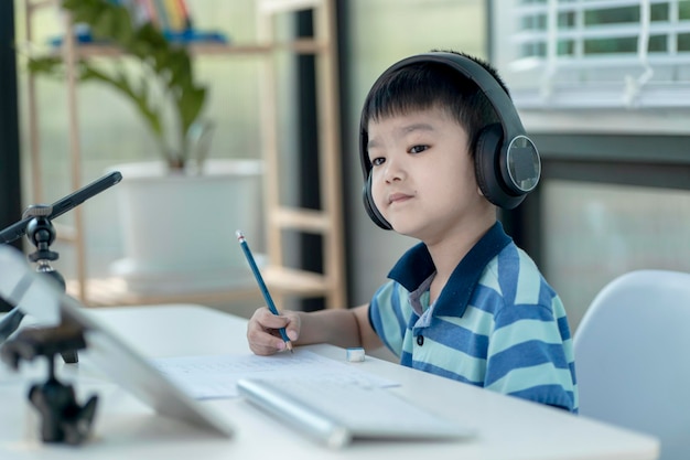 Kinderjunge mit Kopfhörern benutzt ein Tablet und kommuniziert zu Hause im Internet