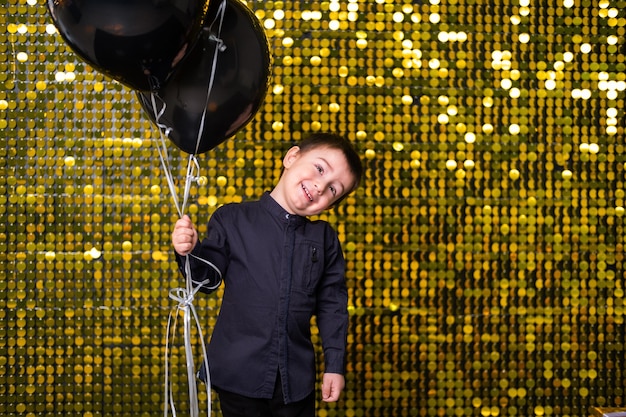 Kinderjunge mit schwarzen Luftballons über goldglänzenden Paillettenpailletten