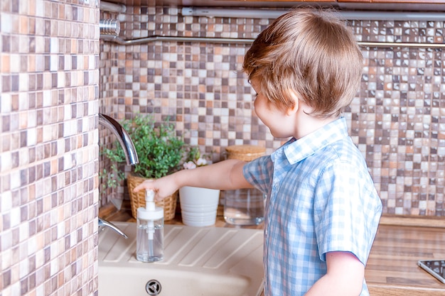 Kinderjunge waschen sich die Hände in brauner Holzspüle mit Pflanze