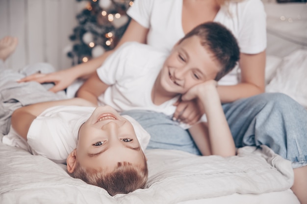 Kinderjungen, die im weißen Schlafzimmer mit Weihnachtsbaum spielen und lachen