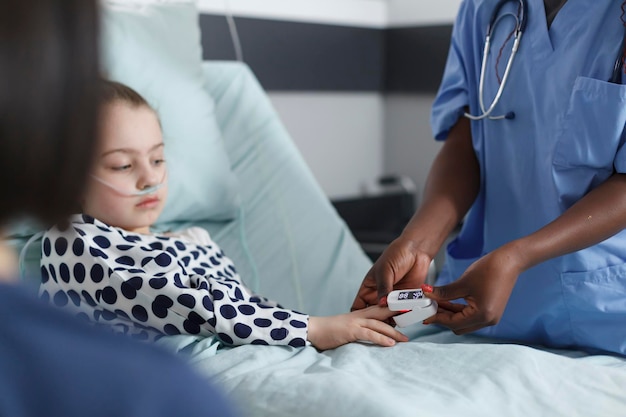 Kinderklinikkrankenschwester, die den Sauerstoffgehalt kranker kleiner Mädchen mit einem Oximeter misst. Medizinisches Krankenhauspersonal misst den Sauerstoffgehalt kranker junger Patienten mit einem Oximeter, während es sich auf dem Bett einer Kinderklinik ausruht.