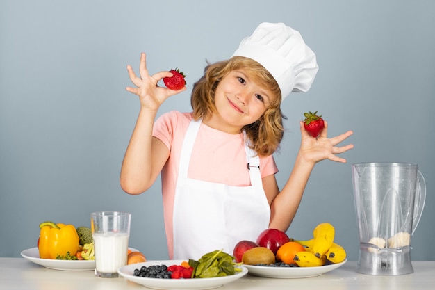 Kinderkoch gekleidete Kochbäckerschürze und Kochmütze halten Erdbeeren isoliert auf Studiohintergrund hea