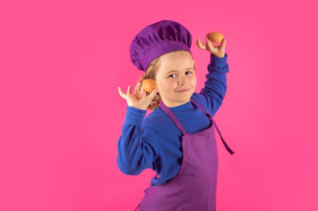 Kinderkoch hält Eier. Kind in Kochuniform und Kochmütze bereitet Essen auf Studio-Farbhintergrund zu. Kocht kulinarisches und Kindernahrungskonzept