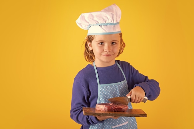 Kinderkoch hält Schneidebrett mit Fleisch, Rindersteak und Messer. Kind in Herduniform und Kochmütze