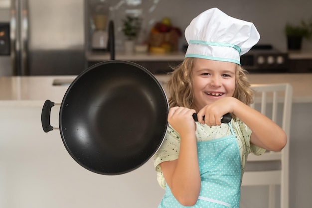 Kinderkoch lernt, wie man einen Kuchen in der heimischen Küche macht Kind macht leckeren, leckeren kleinen Jungen in Kochmütze und eine Schürze, die in der Küche kocht