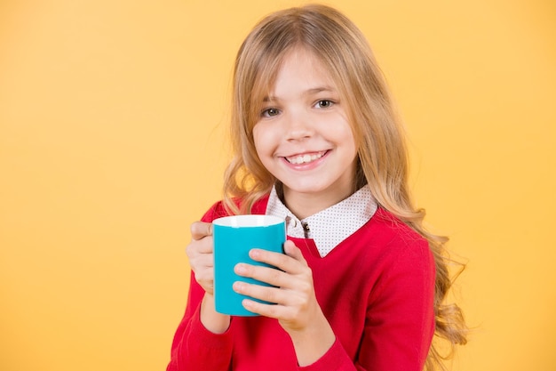 Kinderlächeln mit blauer Tasse auf orangefarbenem Hintergrund