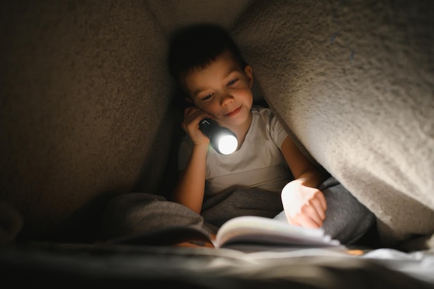 Kinderlesebuch im Bett Kinder lesen nachts Kleiner Junge mit Märchenbüchern im Schlafzimmer Bildung für Kleinkinder Gute-Nacht-Geschichte am Abend Nettes Kind unter Decke im dunklen Raum mit Lampe