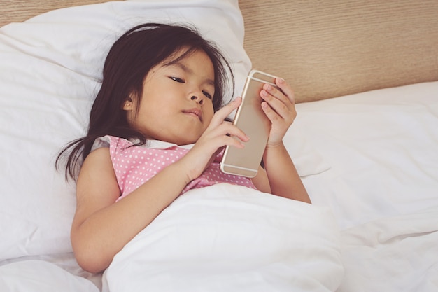 Kindermädchen, das auf Smartphone simst und zu Hause im Bett liegt