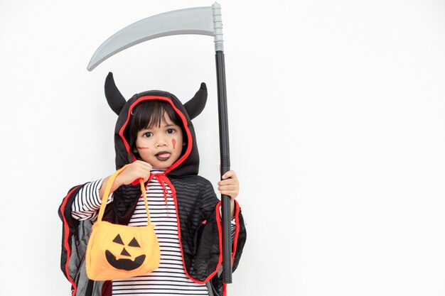 Kindermädchen, das ein mysteriöses Halloween-Kleid trägt, das einen beängstigenden Kürbis und eine Sichel hält.