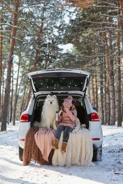 Kindermädchen, das mit ihrem Haustier, einem weißen Hund Samojede im Kofferraum des Autos sitzt