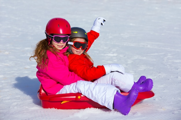 Kindermädchen, die Schlitten im Winterschnee spielen