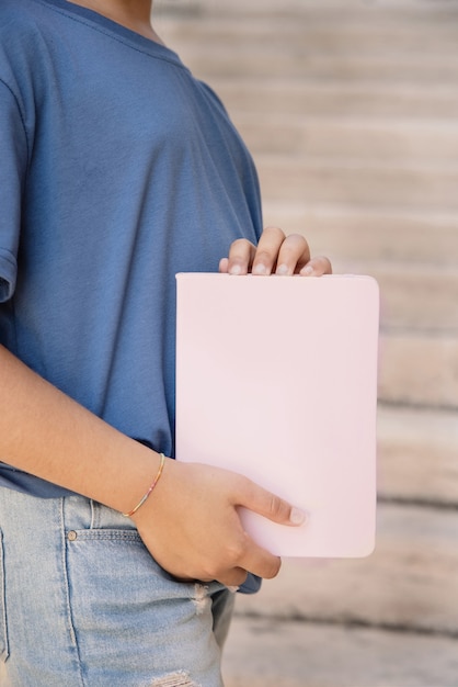 Kindermädchen im blauen T-Shirt, das hellrosa Notizbuch in den Händen steht und hält, Nahaufnahme, beschnittener Schuss. Notebook-Modell