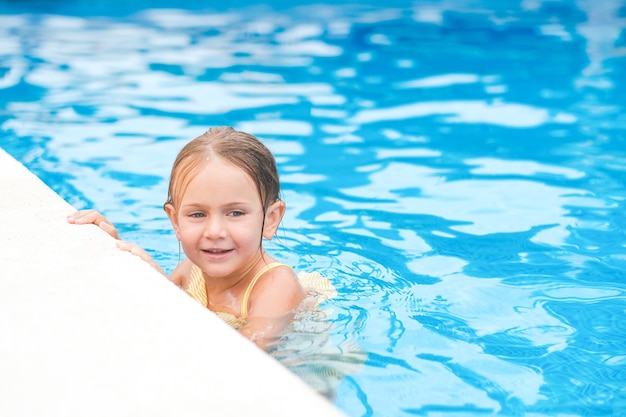 Kindermädchen im gelben Badeanzug schwimmen im Sommerschwimmbad