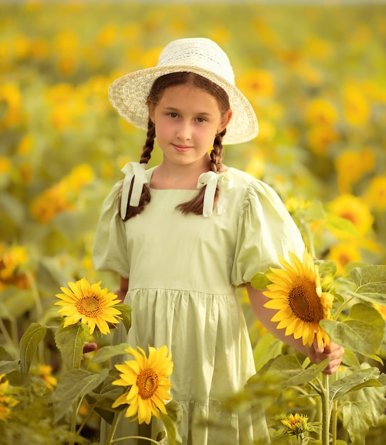 Kindermädchen in grünem Kleid und weißem Hut steht auf einem Feld mit Sonnenblumen