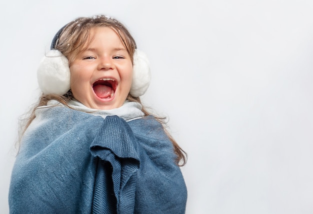 Kindermädchen in Ohrenschützer und warmer Kleidung, die vor Freude auf grauem Hintergrund schreien