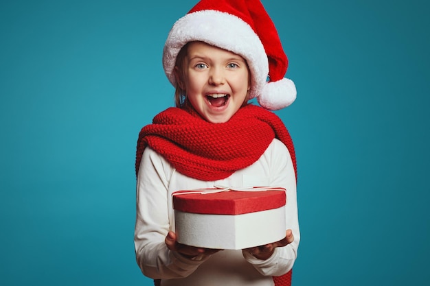 Kindermädchen in Weihnachtsmütze und rotem Schal mit Geschenkbox in Form von