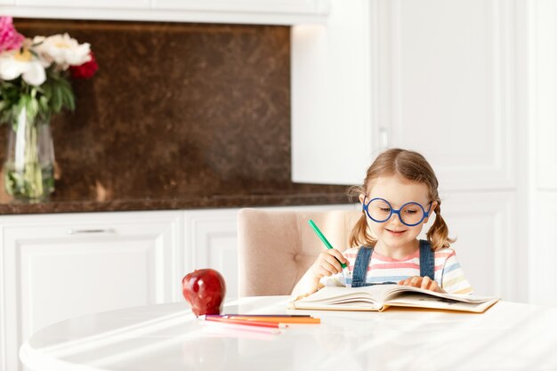 Kindermädchen lernen schreiben, Hausaufgaben machen, sitzen allein am Tisch und machen Notizen, die Buntstifte zeichnen