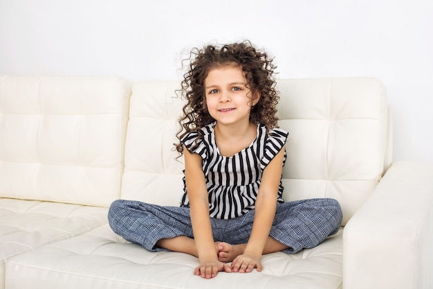 Kindermädchen schön, süß fröhlich und glücklich auf dem weißen Sofa zu Hause modisch