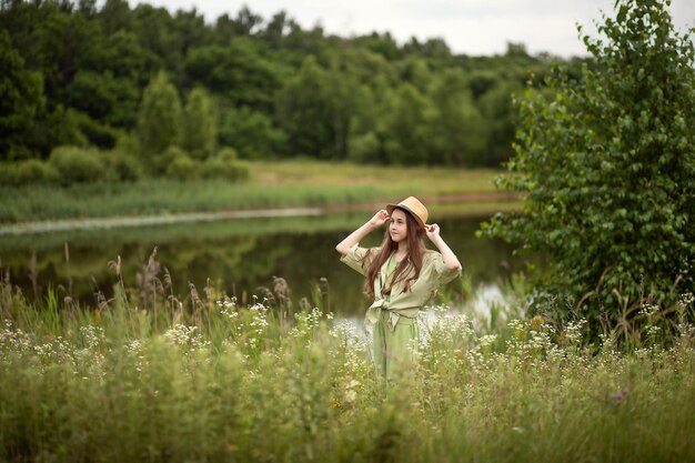 Foto kindermädchen-teenager in grünem anzug und hut steht im gras neben dem see