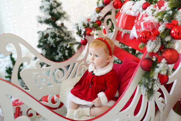 Kindermädchen verkleidet als Weihnachtsmann in der Nähe von Weihnachtsbaum und Geschenken, Winterurlaub im neuen Jahr