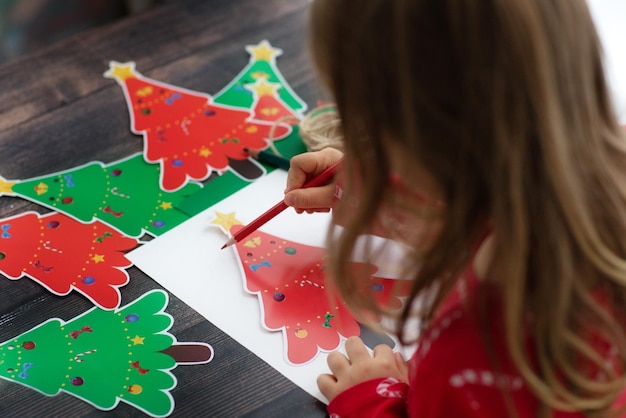 Foto kindermädchen zeichnen und machen weihnachtsgirlande aus handgeschöpftem papier weihnachtsbäume auf holztisch.