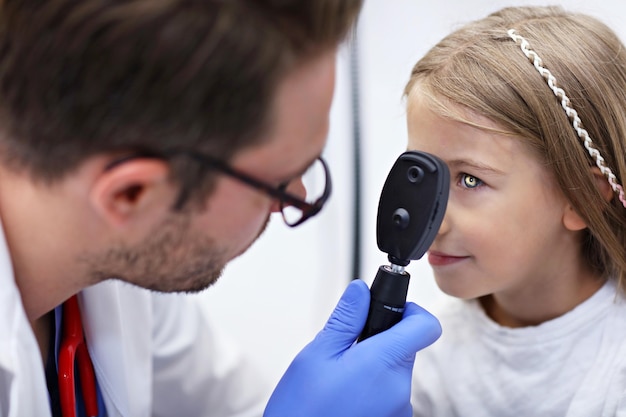 Kinderoptometrie männlicher Optiker Optiker Arzt untersucht das Sehvermögen des kleinen Mädchens