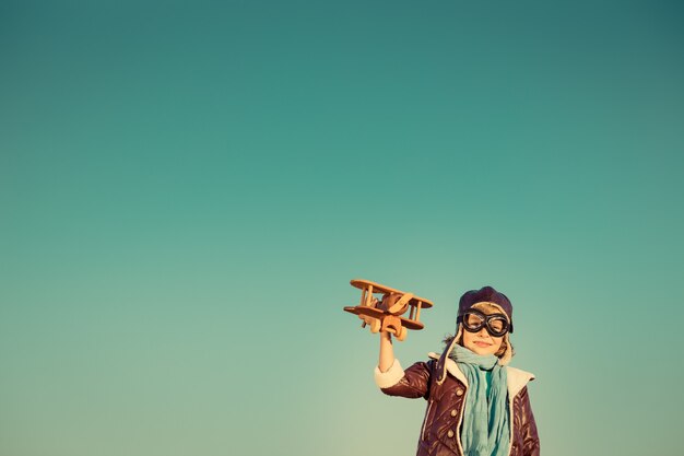 Kinderpilot mit hölzernem Spielzeugflugzeug gegen Herbsthimmelhintergrund Glückliches Kind, das draußen spielt