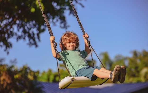 Kinderschaukel auf dem Hinterhofkind, das im Freien spielt, glücklicher süßer kleiner Junge, der schwingt und Spaß hat, gesunde Summe