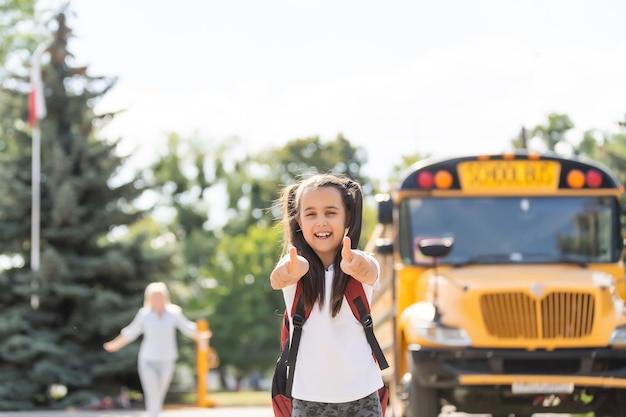 Kinderschüler, der in die hände der mutter rennt, um sie nach der rückkehr zur schule in der nähe des schulbusses zu umarmen